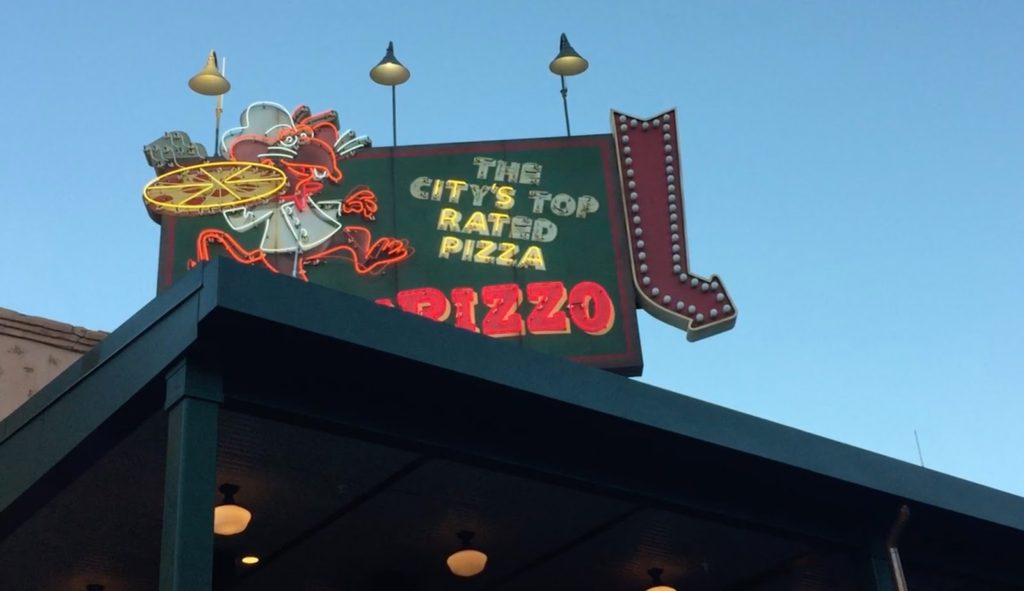 A neon sign reading "THE CITY'S TOP RATED PIZZA," but with particular neon letters unlit so as to spell "IT'S RAT PIZZA"